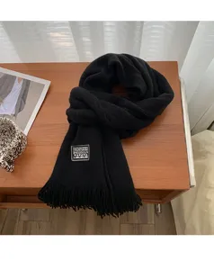Detailed view of the black knit winter scarf with stylish woven label on wooden table.