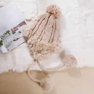 Berretto invernale da trapper in maglia beige con pon-pon e paraorecchie, morbido dettaglio.
