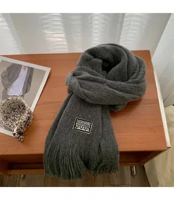 Dark grey knitted scarf detail showing soft texture and woven label design on wooden desk.