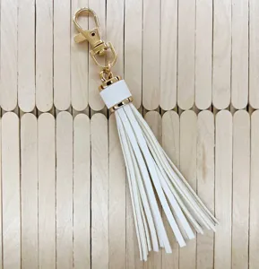 Detailed view of white PU leather tassel keychain featuring gold metal clasp and cap.