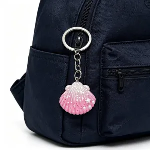 Detail shot of a cute pink glitter seashell keychain hanging on a dark blue backpack.