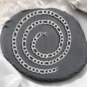 Gros plan sur un collier à chaîne Figaro en argent poli sur une dalle de pierre noire texturée.