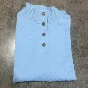 Primo piano di una felpa jacquard azzurra con colletto rialzato e bottoni in metallo