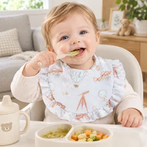Bambino che mangia con un bavaglio in mussola a volant con stampe a tema avventura.