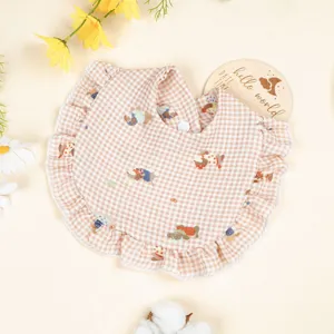 Dettaglio del bavaglino per neonati in cotone vichy beige con volant e stampe di animali.