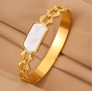 Close-up of a gold stainless steel bangle featuring geometric white shell inlay design