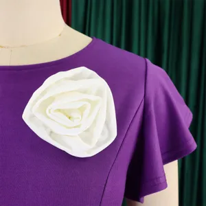 Macro detail of elegant purple dress featuring a large white fabric rose and ruffle sleeves
