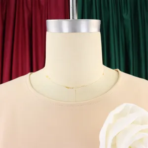 Close-up detail of beige dress crew neckline with white ruffle flower