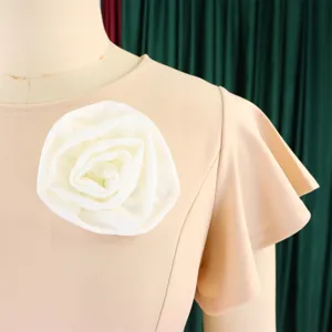 Detailed view of apricot dress featuring a large white flower brooch and ruffle sleeves.