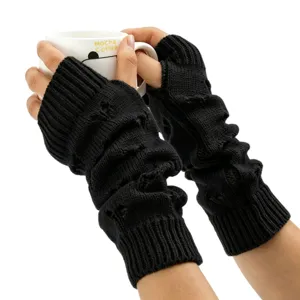Détail des mitaines en tricot noir avec motif cœur tenant une tasse de café blanc.