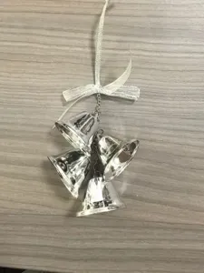 Macro view of four shiny silver metal Christmas bells with a ribbon bow on wood background.