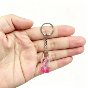 Close-up detail shot of a miniature glass wishing bottle keychain featuring pink sand and liquid.
