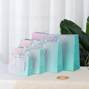 Detail view of pastel gradient paper gift bags with blue ribbons in multiple sizes.