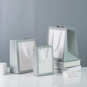 Minimalist green paper gift bags with white ribbon handles, ideal for retail and packaging.