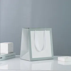 Minimalist light green paper gift bag with white ribbon handles, clean design for boutique use.