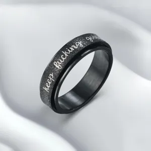 Stainless steel spinner ring detail showing black sandblasted texture and motivational engraving.