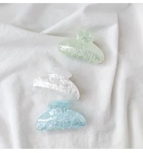 Close-up of three acrylic claw clips in pastel green, white, and blue on white fabric.