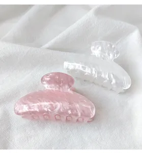 Detailed view of pink and white marble textured acrylic hair claw clips on white fabric