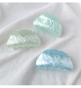 Close-up of minimalist acrylic hair claw clips with marble texture on white fabric
