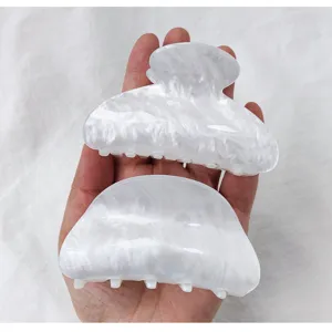 White marble acrylic hair claw clips held in hand showing size and pearly texture