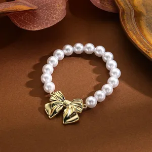 Detalle de una pulsera de perlas blancas con un colgante de lazo dorado metálico