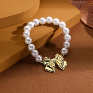Vista detallada de una elegante pulsera de perlas con un dije de lazo dorado metálico.
