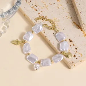 Detalle de pulsera de perlas barrocas con dijes de conchas doradas sobre piedra