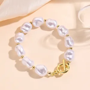 Primer plano de pulsera de perlas barrocas con cierre de oro sobre fondo beige