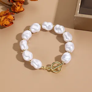 Primer plano de una pulsera de perlas barrocas blancas con cierre de palanca OT dorado.