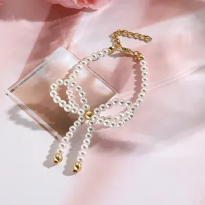 Primer plano de pulsera de perlas blancas con lazo dorado sobre un fondo de seda rosa.