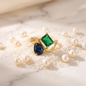 Elegant asymmetrical dual-stone ring with green and blue crystals in gold finish.