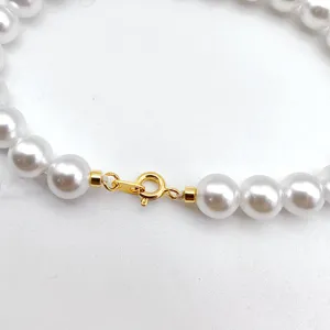 Close-up detail shot of white pearl necklace clasp, gold-plated spring ring lock accessory.