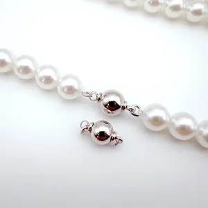 Detail view of a spherical screw clasp for DIY pearl necklaces and bracelets, shiny metallic.