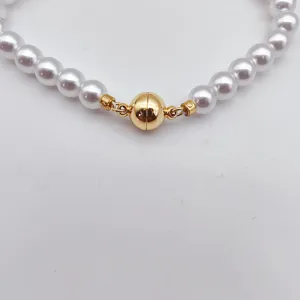 Close-up detail of the gold spherical magnetic clasp and white pearl necklace, shiny finish.