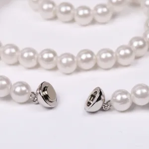 Close-up detail of white faux pearl necklace and bracelet magnetic clasp connector hardware.