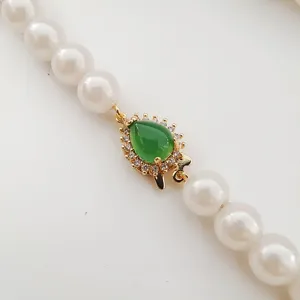 Pearl necklace clasp detail showcasing a gold-plated fishhook with green stone and cubic zirconia.