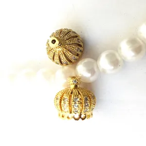 Gold crown jewelry pendant accessory with sparkling stones paired with white pearl chain details.