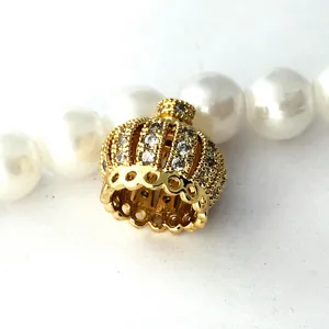 Detailed shot of gold plated crown jewelry clasp inlaid with sparkling stones near pearls.