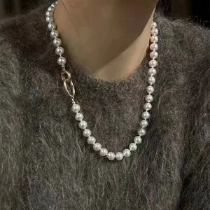 Detail shot of a pearl necklace featuring a distinctive metal clasp worn on a grey sweater.
