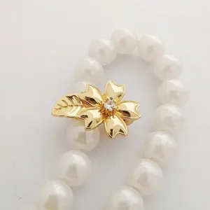 Close up view of gold plated flower leaf jewelry clasp with white pearl necklace beads detail