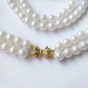 Close-up detail shot of a double-layer pearl necklace with a shiny gold bow rhinestone clasp.