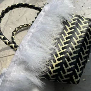 Bolso de mano tejido en blanco y negro con ribete de plumas blancas y asa trenzada.