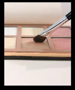 Detailaufnahme eines Papierschminkpinsels beim Auftragen von Lidschatten aus einer Palette für Nasen.