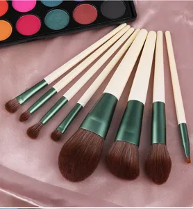 Close up of 8 piece makeup brush set with green ferrules and soft brown bristles on silk.