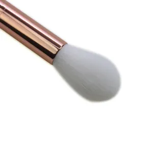 Close-up detail of soft makeup brush with rose gold ferrule and white bristles for highlighting.