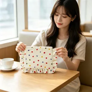 Close-up detail of cute polka dot cosmetic bag with ruffled edge held by model hands.
