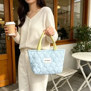 Close-up detail shot of the light blue quilted handbag featuring yellow handles in cafe scene.