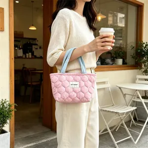 Detailed view of the quilted pink lunch handbag with blue handles and brand tag in cafe.