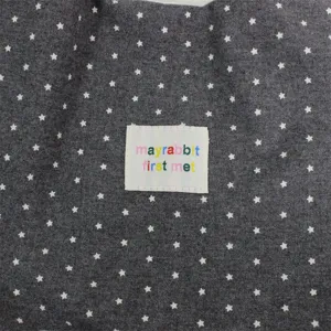Close-up of dark grey star print canvas tote bag fabric with embroidered tag detail.