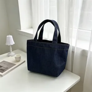 Vista detallada del bolso tote de mezclilla azul oscuro, mini bolso minimalista en escritorio blanco.